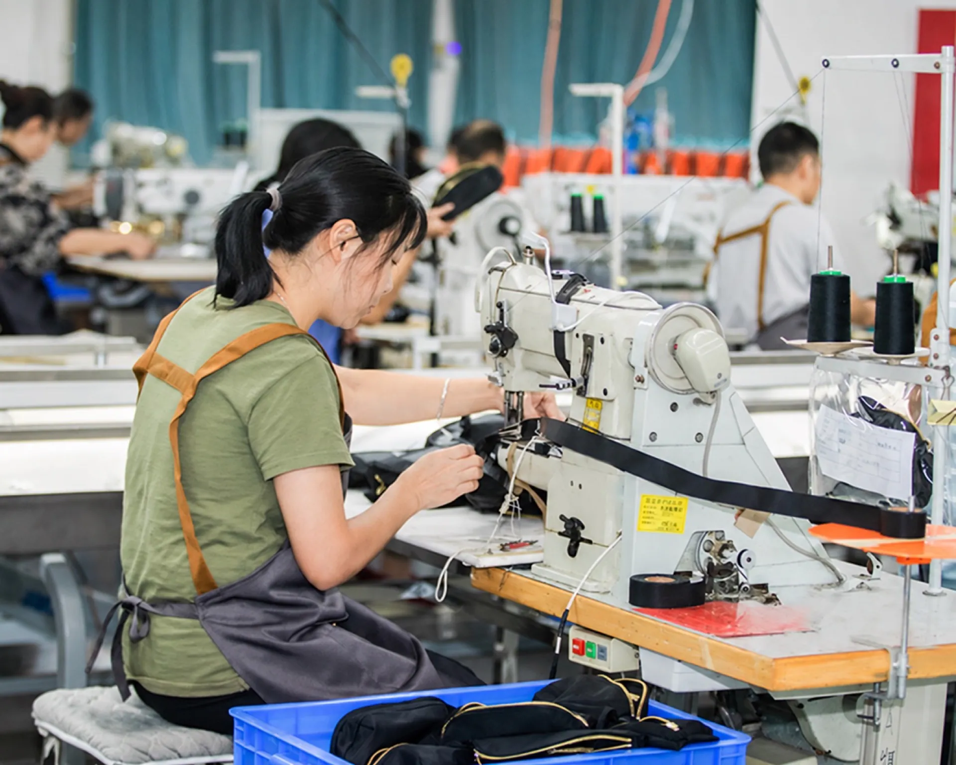 Garment worker guiding material through an industrial sewing machine